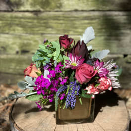 Mixed bouquet with pink roses, purple blooms, and a square glass vase