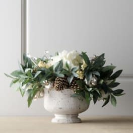 White floral arrangement in a pedestal urn with greenery and pinecones