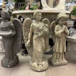 Three angel statues displayed in a store, with a small floral arrangement on a table behind them.