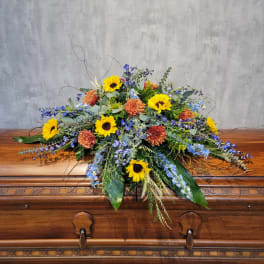 Large floral spray with sunflowers and orange blooms on a casket