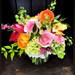 Colorful bouquet of roses, ranunculus, and orchids in a glass vase