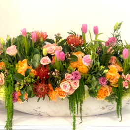 Large mixed floral arrangement with pink tulips and roses in a white bowl