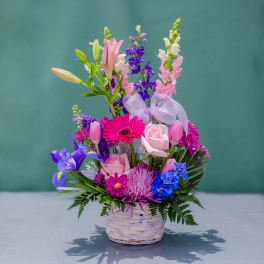 Mixed bouquet in a woven basket with pink, purple, and blue flowers