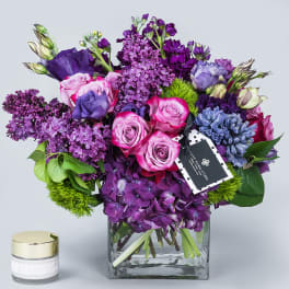 Purple and pink bouquet in a square glass vase with a small candle beside it
