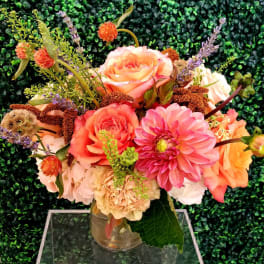 Mixed bouquet of peach, pink, and cream flowers in a clear glass vase