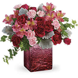 Red and pink roses, carnations, and alstroemeria in a red glass cube vase with trailing ivy