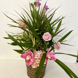 Pink orchids and roses in a woven basket with long green leaves