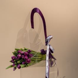 Purple tulips in a clear handbag-shaped container with a ribbon handle