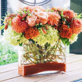 Orange and peach floral arrangement in a clear rectangular vase