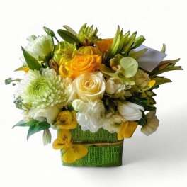 Compact yellow and white flower arrangement with roses in a green fabric-wrapped cube vase