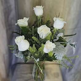 White roses arranged in a glass vase with silvery foliage