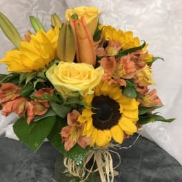 Bouquet of yellow roses, sunflowers, and peach alstroemeria in a glass vase