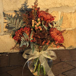 Orange chrysanthemum bouquet in a glass vase with a gold ribbon
