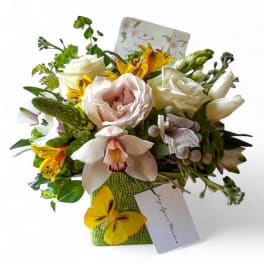 Compact bouquet of white and blush flowers with yellow accents in a green cube vase with a butterfly decoration.