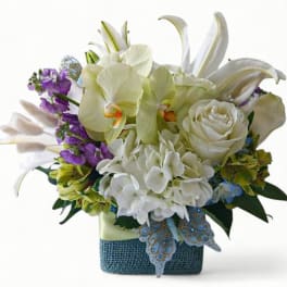 Compact arrangement of white lilies, orchids, hydrangeas, and roses in a blue square vase
