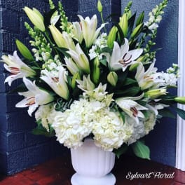 White lilies and hydrangeas arranged in a white urn vase