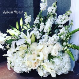 White floral arrangement with lilies, roses, and tall white blooms in a black container