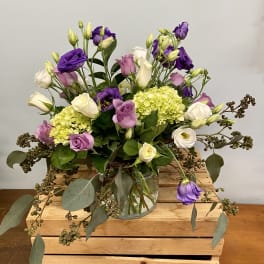 Purple and white flowers in a glass vase with trailing greenery
