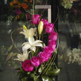 Pink roses and white lilies in a tall black container with curly branches