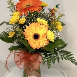 Orange and yellow gerbera daisies in a glass vase with a ribbon