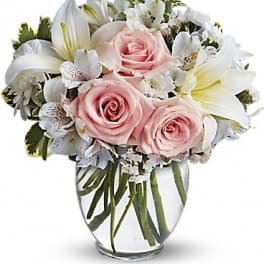 Round vase of light pink roses and white lilies with other white flowers