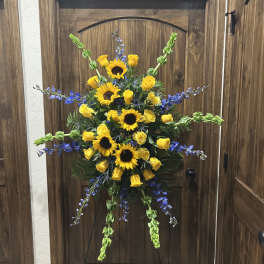 Standing floral spray with yellow sunflowers and roses accented by blue flowers