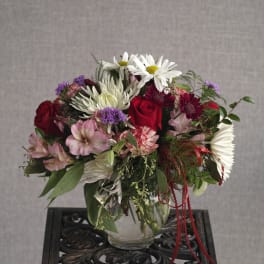 Mixed bouquet of red roses, white daisies, and pink flowers in a glass vase