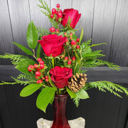 Red roses arranged in a red vase with berries and a pinecone