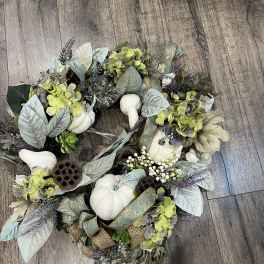 Decorative wreath with white pumpkins, hydrangeas, and ribbon on a wood floor