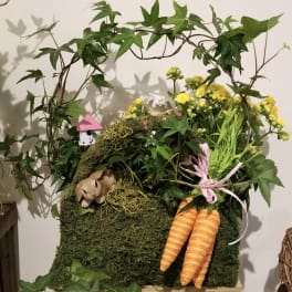 Moss-covered arrangement with yellow flowers, ivy, and two orange carrots