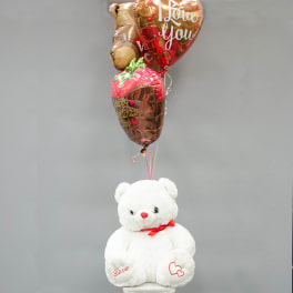White teddy bear with heart-shaped balloons above it