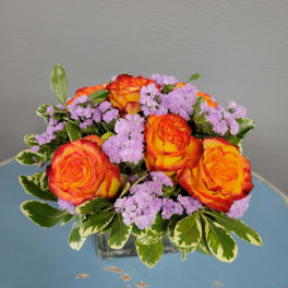 Orange roses and lavender filler flowers in a square glass vase