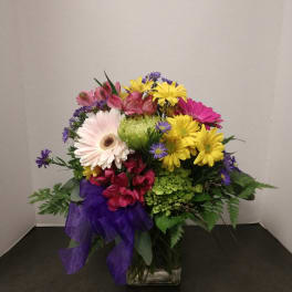 Mixed bouquet of daisies and alstroemeria in a glass vase with a purple ribbon