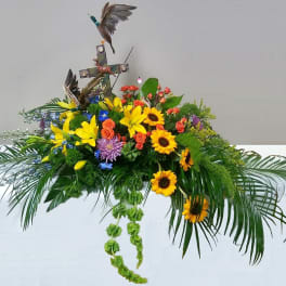 Floral arrangement with sunflowers, lilies, and a cross topper