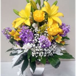 Yellow lilies and purple flowers in a silver vase