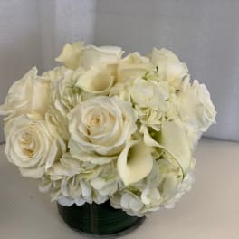 White roses and calla lilies arranged in a low dark vase