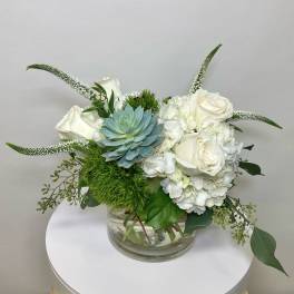 White roses and hydrangeas in a glass vase with a blue succulent
