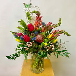 Tall mixed bouquet in a clear glass vase with bright pink, yellow, and blue flowers