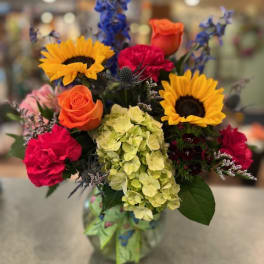 Mixed bouquet with sunflowers, roses, hydrangea, and carnations in a glass vase
