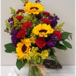 Bouquet of sunflowers, red carnations, and purple flowers in a glass vase