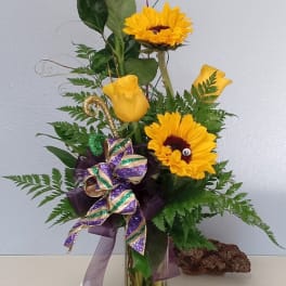 Yellow roses and sunflowers in a tall glass vase with a ribbon bow