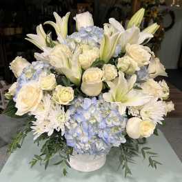 White lilies, roses, and blue hydrangeas arranged in a white vase