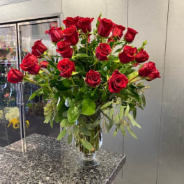 Tall vase arrangement of red roses with greenery