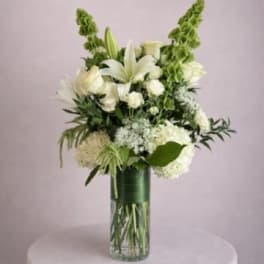 White lilies and hydrangeas in a tall glass vase with green accents