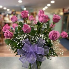 Pink roses in a glass vase with a purple bow