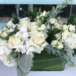 White rose and orchid arrangement in a green rectangular vase