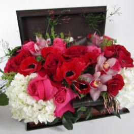 Mixed bouquet of red and pink roses with white hydrangeas and orchids in a dark box