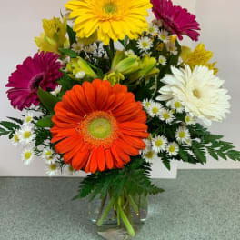 Mixed bouquet of bright gerbera daisies and small white daisies in a clear glass vase