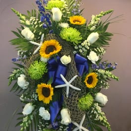 Large floral standing spray with sunflowers, white roses, and blue ribbon