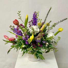 Mixed bouquet of tulips, lilies, and purple flowers in a white vase